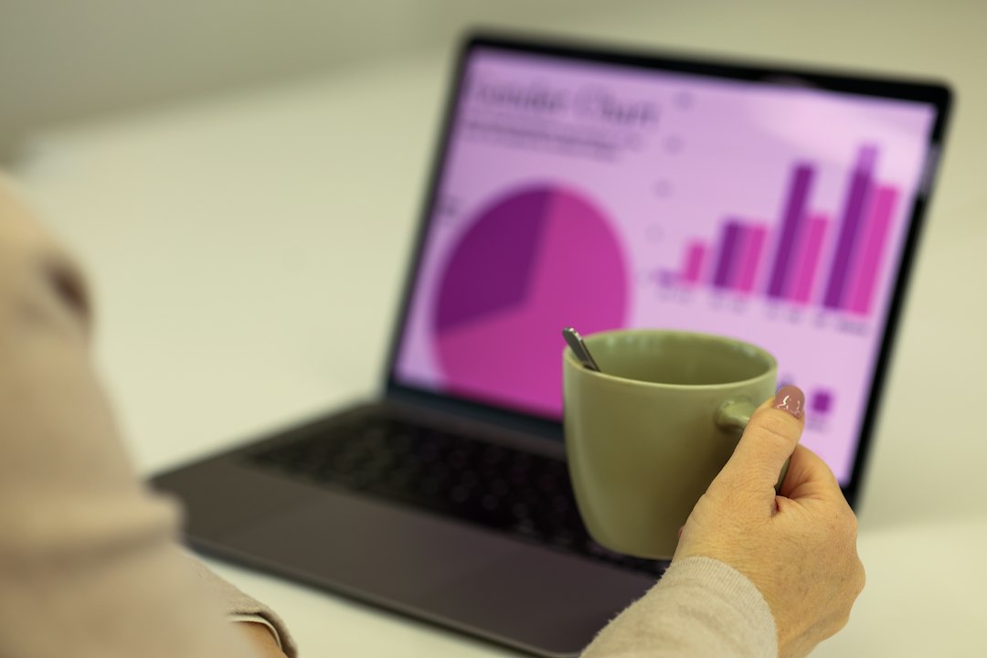 Person holding a coffee mug while reviewing charts and graphs on a laptop screen
