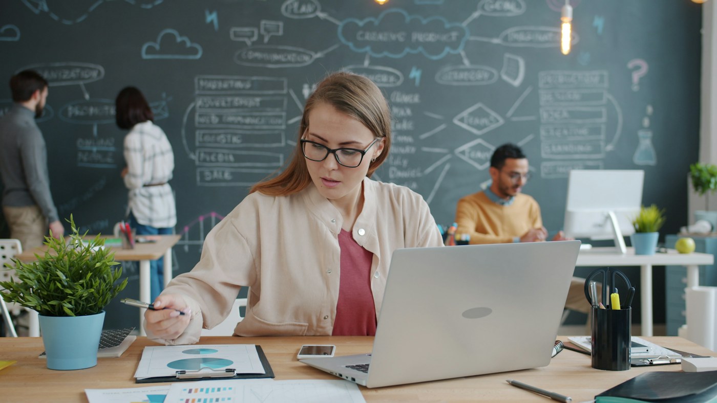 Employee using a laptop with coworkers collaborating in the background, representing enterprise AI adoption