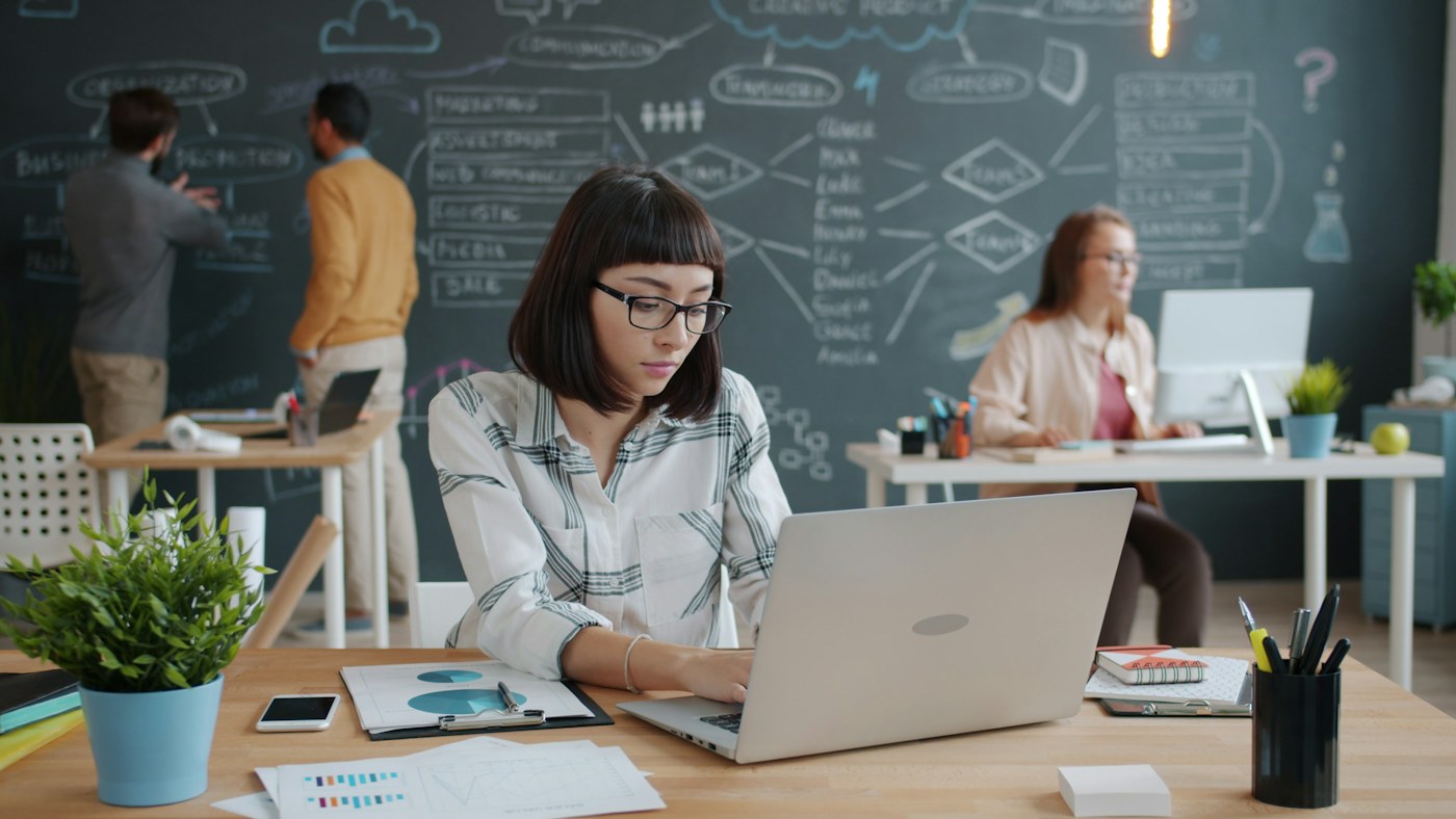 Professional working on a laptop in a shared office, representing AI access inside everyday work tools