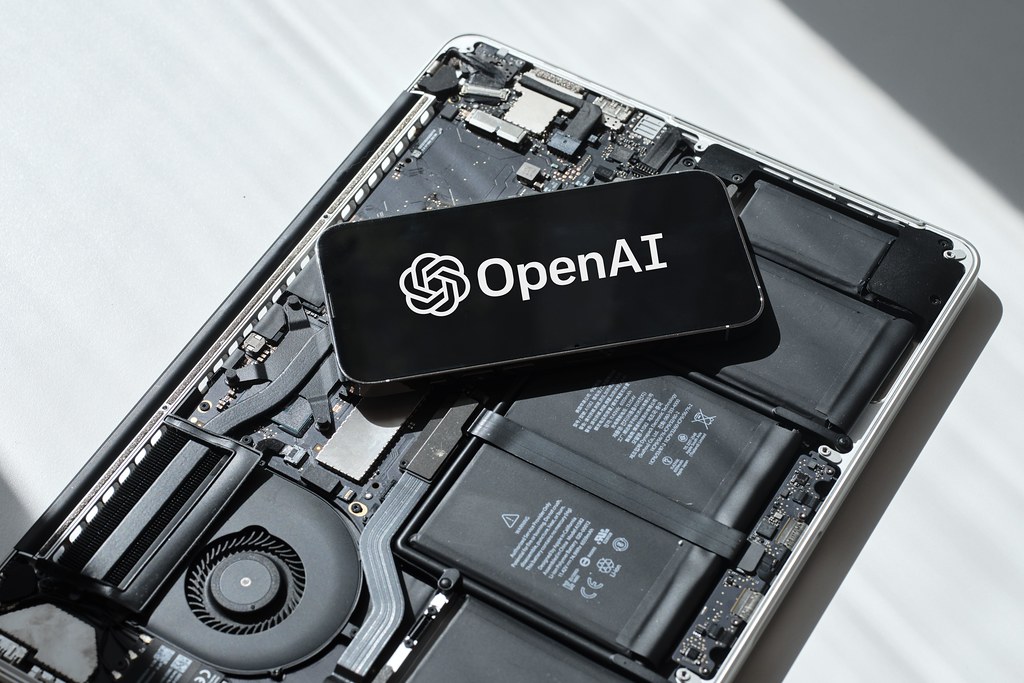 Smartphone displaying the OpenAI logo resting on exposed laptop components