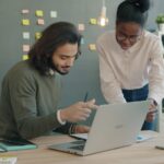 Two coworkers reviewing documents and a laptop, representing AIforce CRM collaboration